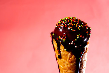 Ice cream with chocolate topping in waffle cone at pink background