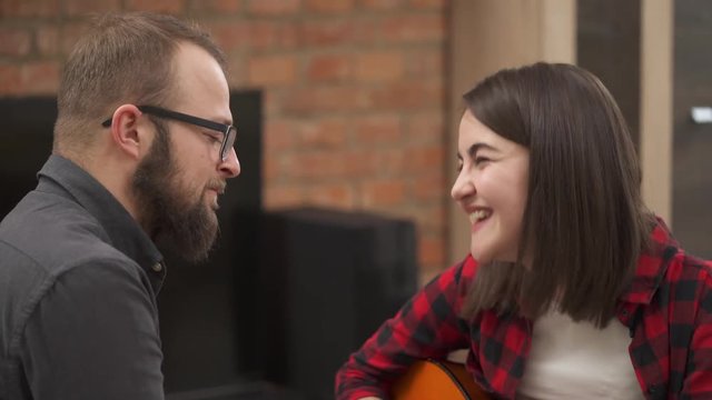 Close-up of a young couple singing and having fun together. A beautiful girl plays an acoustic guitar and her boyfriend dances and imitates playing drums.