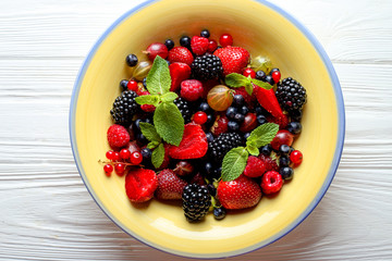 Fruit salad with raspberry, currant, strawberry, blueberries, gooseberries, blackberries and mint on a yellow plate.