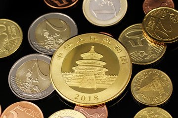 A macro image of an assortment of Euro coins and a gold Chinese one ounce coin on a reflective...