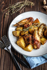 Baked chicken wings with potatoes and garlic on a rustic background