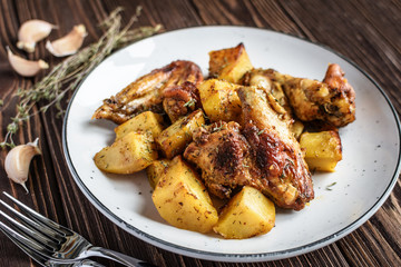 Baked chicken wings with potatoes and garlic on a rustic background