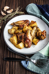 Baked chicken wings with potatoes and garlic on a rustic background