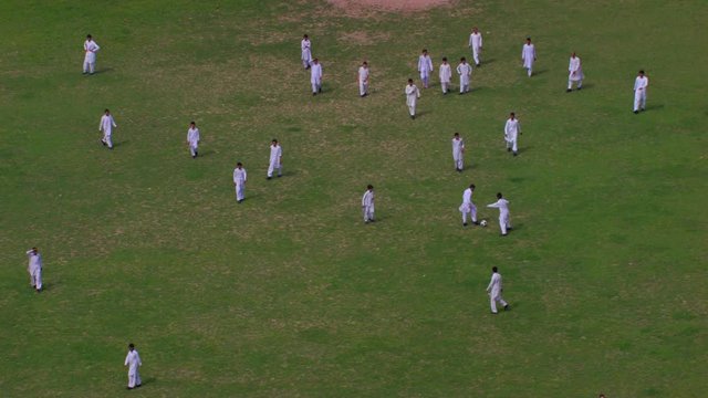 Peshawar, Pakistan, students playing foot ball aerial view from the trees, Students are in white shalwar kameez uniforms, grass in the ground