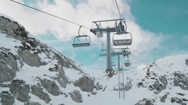 POV view travelling on ski resort lift uphill to mountain peaks. Blue sky upward view.