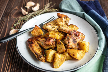Baked chicken wings with potatoes and garlic on a rustic background