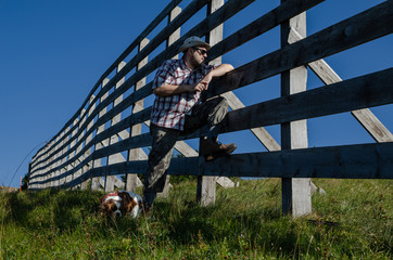 Farmer leaned on a wooden fence and his dog