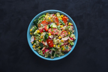 Salad with quinoa and corn on a black table.