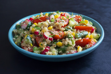 Salad with quinoa and corn on a black table.