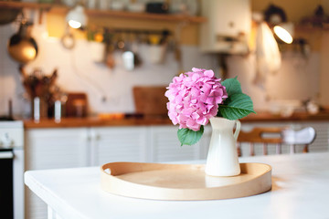 Pink hydrangea flower on wooden serving tray. Morning kitchen scene. Cozy home atmosphere hygge. Spring still life on table for Women Day.
