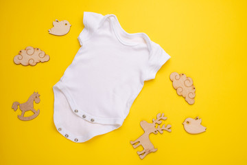 mockup Flat Lay a white baby shirt with wooden toys on a yellow background. Layout for the design and placement of logos, advertising, children's party baby shower, children's birthday
