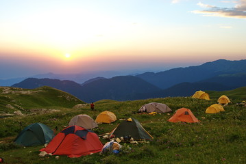 Camping tents on a green meadow in the mountains at sunset. Expedition life. Bright and colorful tent on the meadow. Active lifestyle. Sport equipment.