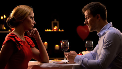 Disappointed woman looking at boyfriend using smartphone during romantic date