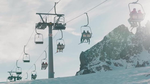Skiers travelling on chair lifts at ski resort. Sun light leaks from right side of frame.