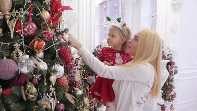 A woman holding a little daughter in her arms at a decorated Christmas tree.