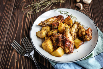 Baked chicken wings with potatoes and garlic on a rustic background