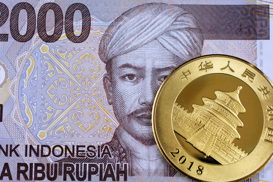 A close up image of an Indonesian two thousand rupiah note with a Chinese one ounce golden panda coin