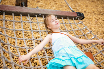 Blonde girl in white and blue dress playing in the playground in the summer park of entertainments