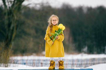 Funny little girl in big adudlt oversized yellow woolen shirt and yellow boots holding bpuquet of...