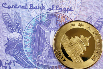 A close up image of a shiny Chinese gold coin with an Egyptian twenty five piastre bank note