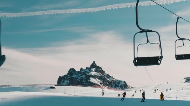 Ski lift chairs passing in shot as skiers travel the slopes below.