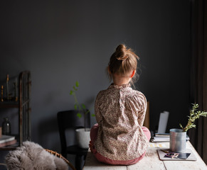 Rear view of girl sitting on table at home