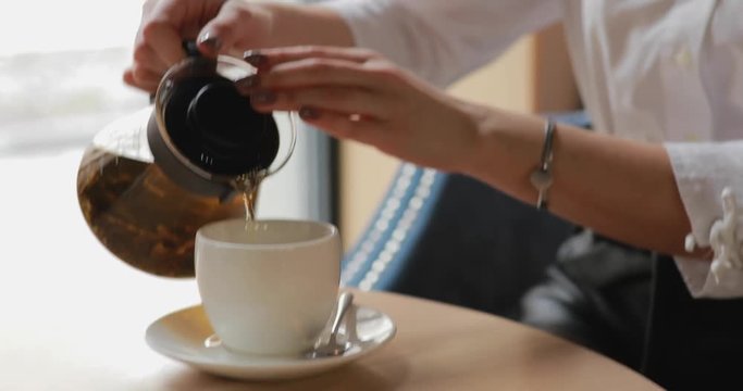 Woman pours tea into cup sitting in a cafe