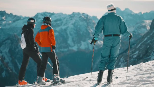 Thee skiers on top of ski resort snowy peaks, looking out to horizon mountain range.
