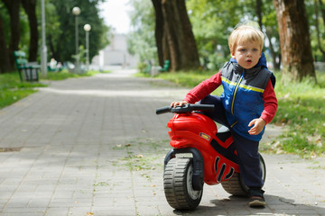 Fototapeta na wymiar Cute Baby Boy Sitting On A toy Motorcycle in the park. copy space