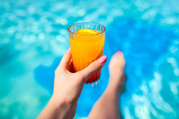 Woman holds a cocktail on swimming pool background. All inclusive