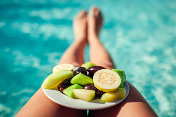 Woman holds plate with fruits on swimming pool background. All inclusive
