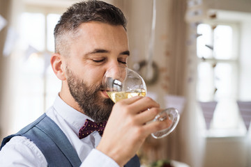 A portrait of mature man indoors in a room set for a party, drinking wine.