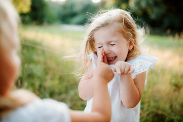 Two small girl friends or sister playing outdoors in sunny summer nature.