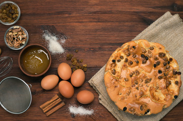 Apple pie (charlotte) with raisins, apples, walnuts and lemon zest on a brown wooden surface. Next to the ingredients for making the cake