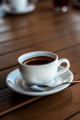 A small white porcelain espresso cup on a saucer with a teaspoon and two pieces of sugar