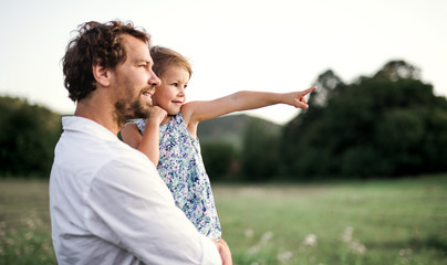 Young father in nature holding small daughter in the arms. Copy space.