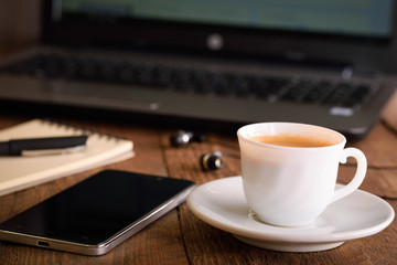  Laptop (notebook) mobile phone (smartphone) and notepad with pen on old wooden table. Work place modern.Cup of coffee