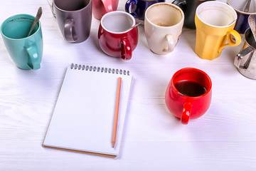 Empty dirty coffee cups, different colors on the table and a notebook for writing a letter. Concept caffeine dope, lack of energy to solve the problem. Copy space.