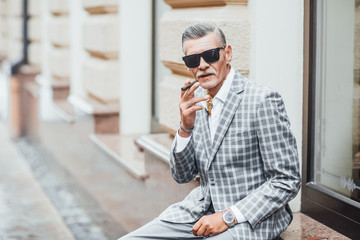 One stylish old man smoking cigarette ,wearing at gray suit .Close up