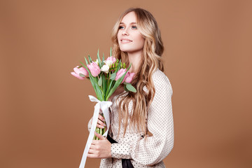 Happy beautiful elegant woman with pink bouquet of tulips over beige background.