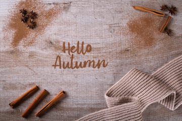 Hello, Autumn. The phrase is written on a wooden table with ground cinnamon among cinnamon sticks and badyan.  Top view, flat lay