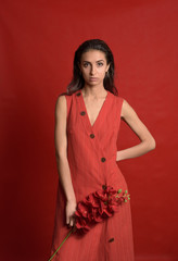 Fototapeta premium Fashion Woman wearing a red dress holding a red orchid against red background