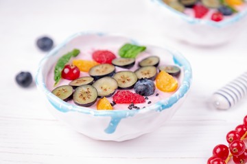 Ceramic bowl with whipped quark mousse and raspberries, blueberries, red currant and winter cherry on a white background