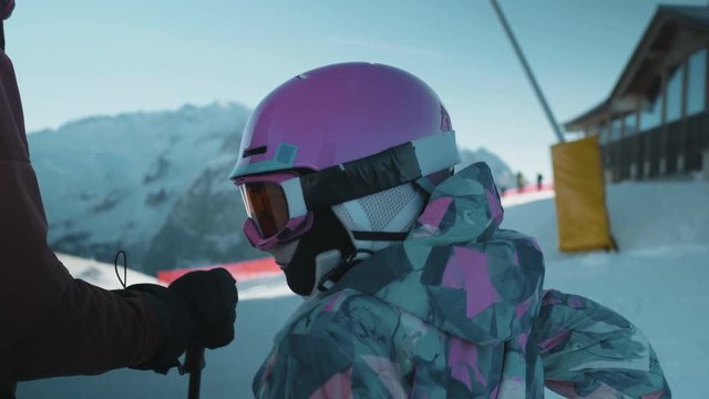 Rear view of little girl in ski gear on top of slopes. Skiers travelling downhill in background.