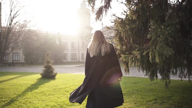 A young beautiful woman whirling back and forth, walking with her yearling baby in a sling in front of an old castle