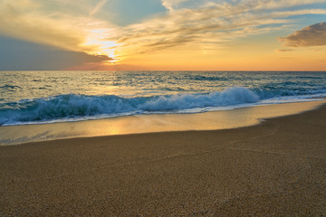 Fototapeta premium Tropical sandy beach. Sunset seascape. Waves with foam hitting sand.