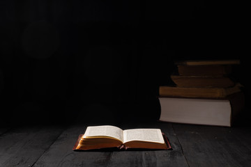 Open book of Bible on dark table. Low-key image of New Testament in bright light among darkness and...