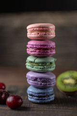 Beautiful and tasty French macaroon cookies stand on a wooden stand next to the fruit. Romantic dinner in the back of the house. Fast food menu background.