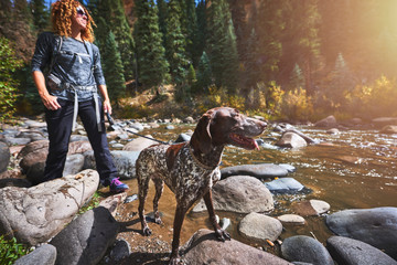 a young woman and her dog hiking next to a mountain stream.
