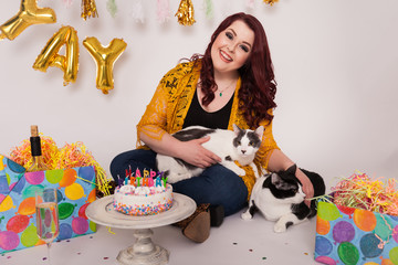 Obraz na płótnie Canvas Cute young lady smiling with two cats birthday decorations birthday themed gifts and cake 